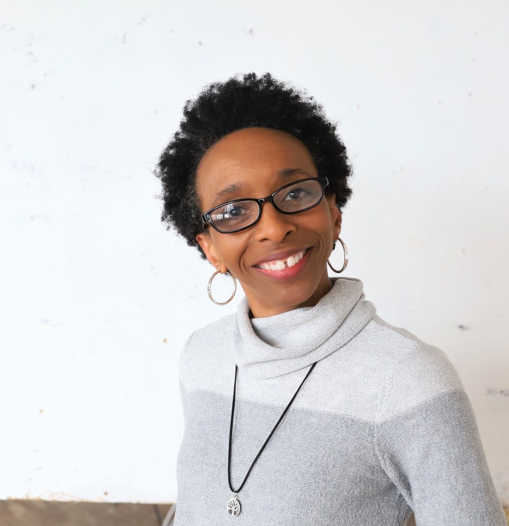 Smiling Black woman with glasses, hoop earrings, and short natural hair