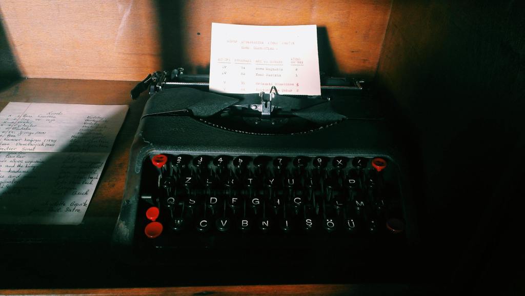 Black typewriter with red keys sitting on wooden surface.